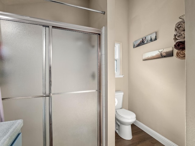 bathroom featuring baseboards, a shower with shower door, toilet, and wood finished floors