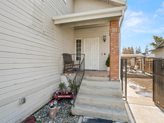 entrance to property featuring a patio, brick siding, and fence