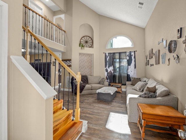 living room with a textured ceiling, high vaulted ceiling, wood finished floors, visible vents, and stairway