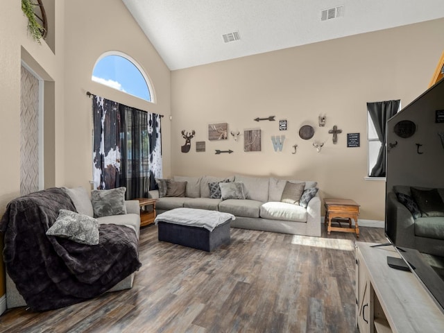 living area featuring high vaulted ceiling, wood finished floors, visible vents, and baseboards