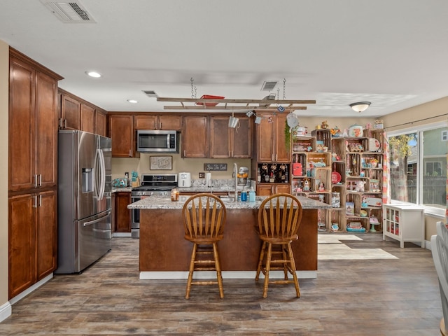 kitchen featuring light stone counters, stainless steel appliances, visible vents, dark wood-type flooring, and a kitchen island with sink