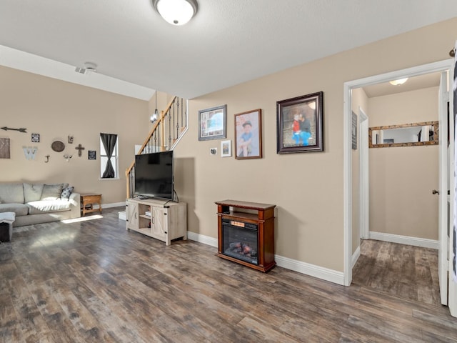 unfurnished living room with baseboards, stairway, wood finished floors, and a glass covered fireplace