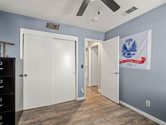 bedroom with baseboards, visible vents, a ceiling fan, wood finished floors, and a closet