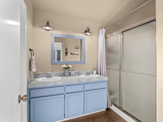 full bath featuring double vanity, a sink, a shower stall, and wood finished floors