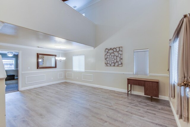 empty room with a notable chandelier, crown molding, light wood-style flooring, and a high ceiling