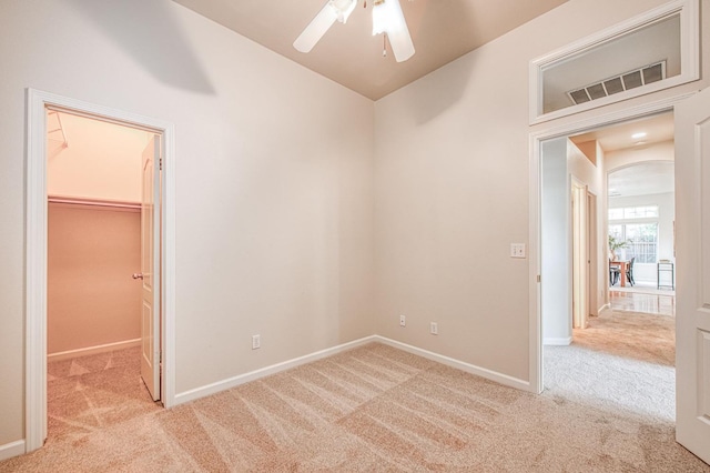 carpeted empty room with arched walkways, ceiling fan, visible vents, and baseboards