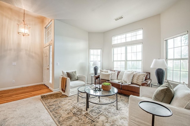 living area with visible vents, a high ceiling, an inviting chandelier, wood finished floors, and baseboards