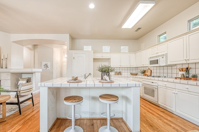 kitchen featuring tile countertops, white appliances, visible vents, and a kitchen breakfast bar