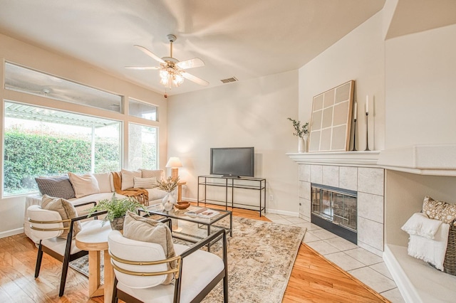 living room with baseboards, a ceiling fan, a tiled fireplace, and wood finished floors