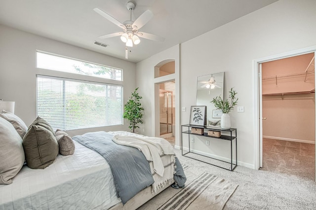 bedroom with carpet floors, a ceiling fan, visible vents, baseboards, and a walk in closet