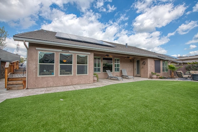 back of property with a yard, a patio, solar panels, stucco siding, and ceiling fan