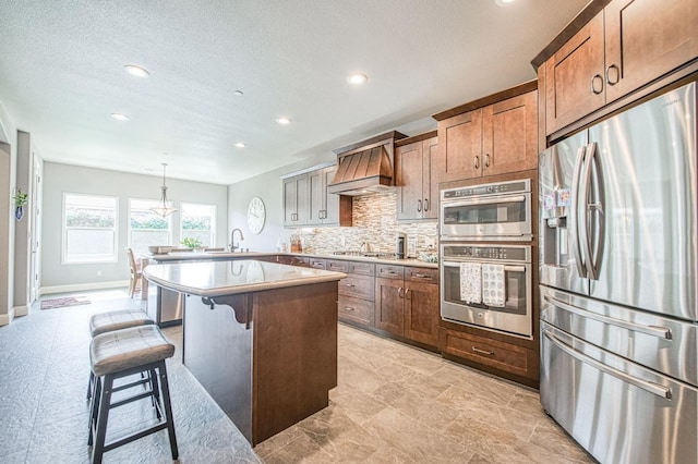 kitchen with decorative backsplash, a breakfast bar area, appliances with stainless steel finishes, premium range hood, and a sink