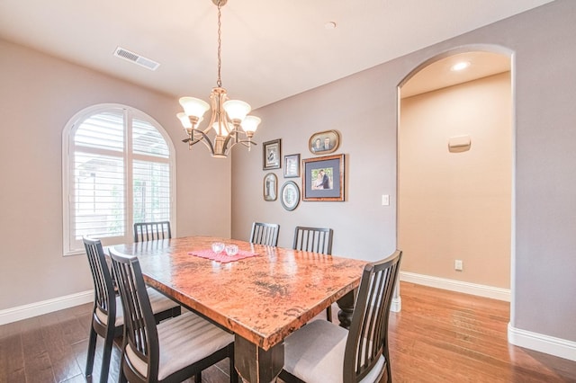 dining area featuring baseboards, visible vents, arched walkways, wood finished floors, and a chandelier