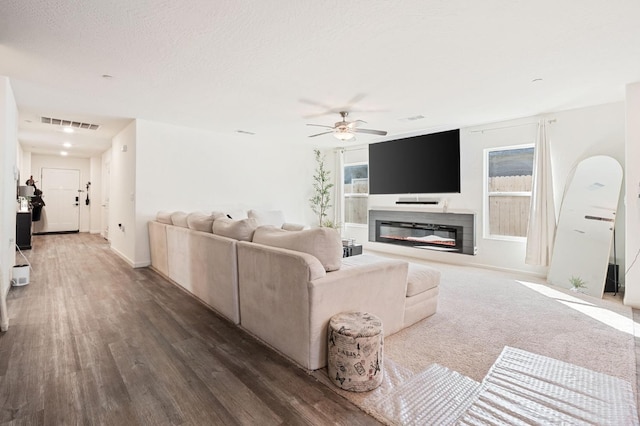 living room with visible vents, a ceiling fan, a glass covered fireplace, wood finished floors, and a textured ceiling