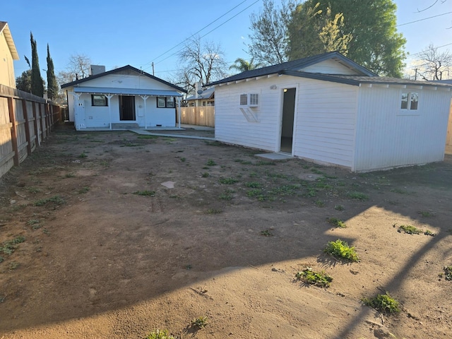 rear view of property featuring an outdoor structure and fence