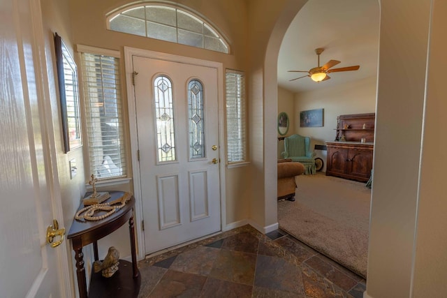 foyer featuring arched walkways, stone tile flooring, ceiling fan, and baseboards