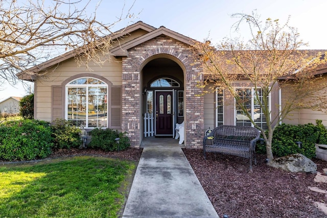 entrance to property with brick siding and a yard