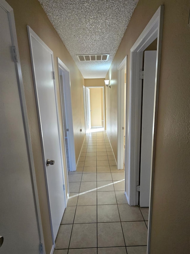 corridor featuring visible vents, a textured ceiling, baseboards, and light tile patterned flooring