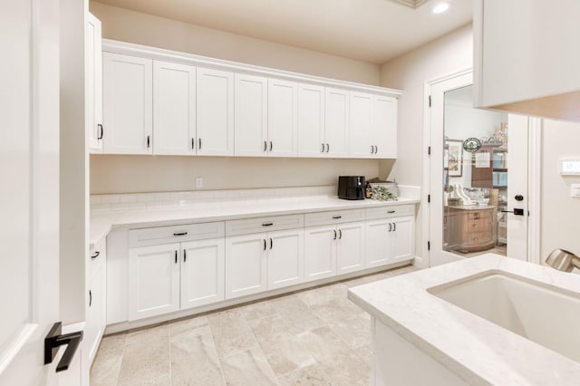 kitchen with light stone counters, white cabinets, a sink, and recessed lighting