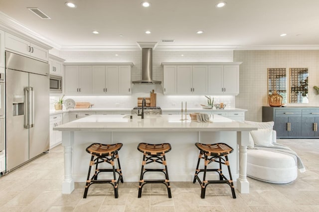 kitchen featuring built in appliances, visible vents, wall chimney range hood, a kitchen bar, and crown molding