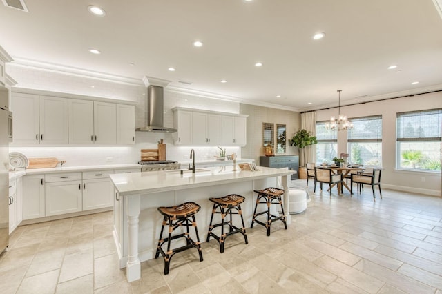 kitchen featuring wall chimney exhaust hood, light countertops, backsplash, ornamental molding, and a kitchen breakfast bar