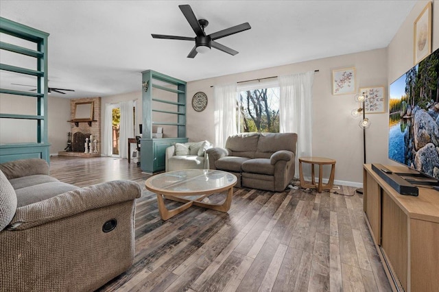 living area with a brick fireplace, ceiling fan, baseboards, and wood finished floors