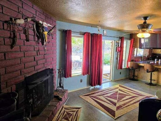 living room with a ceiling fan, a brick fireplace, and a textured ceiling