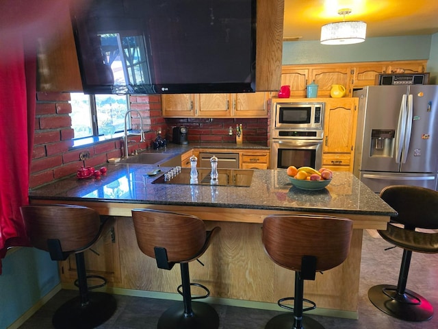 kitchen with dark stone counters, appliances with stainless steel finishes, a peninsula, a sink, and backsplash