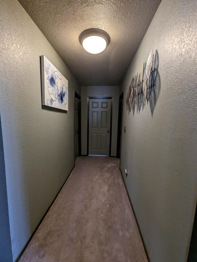 corridor featuring a textured wall, carpet floors, and a textured ceiling