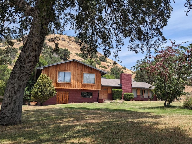 tri-level home with brick siding, a mountain view, a chimney, and a front lawn