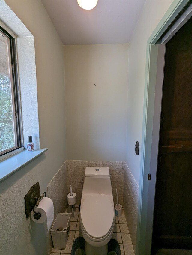 bathroom featuring toilet, a wainscoted wall, tile walls, and tile patterned floors