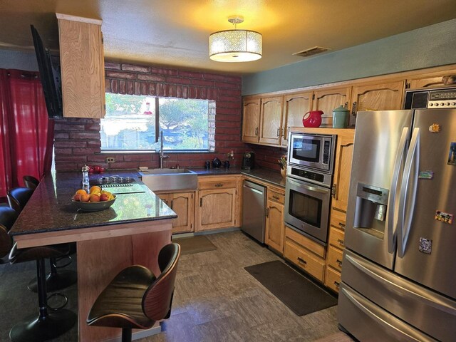 kitchen featuring visible vents, appliances with stainless steel finishes, a breakfast bar, a peninsula, and a sink