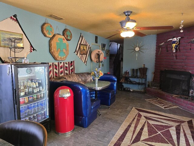 recreation room featuring ceiling fan, a textured ceiling, a brick fireplace, and visible vents