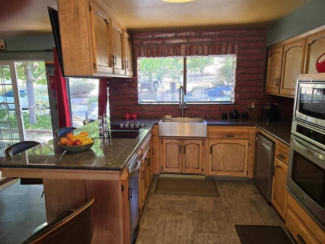 kitchen featuring stainless steel appliances, brown cabinets, a sink, and a textured ceiling