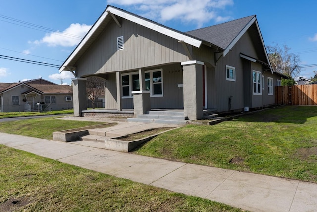 bungalow-style home featuring a porch, roof with shingles, fence, and a front lawn