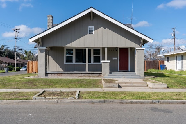 bungalow-style home with covered porch, a chimney, a front yard, and fence