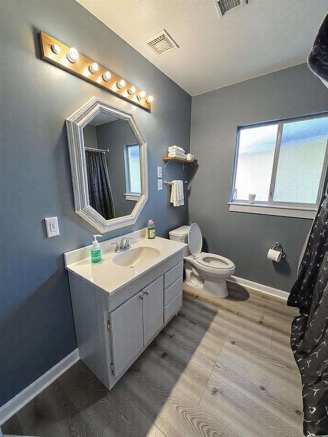 bathroom featuring wood finish floors, baseboards, visible vents, and toilet