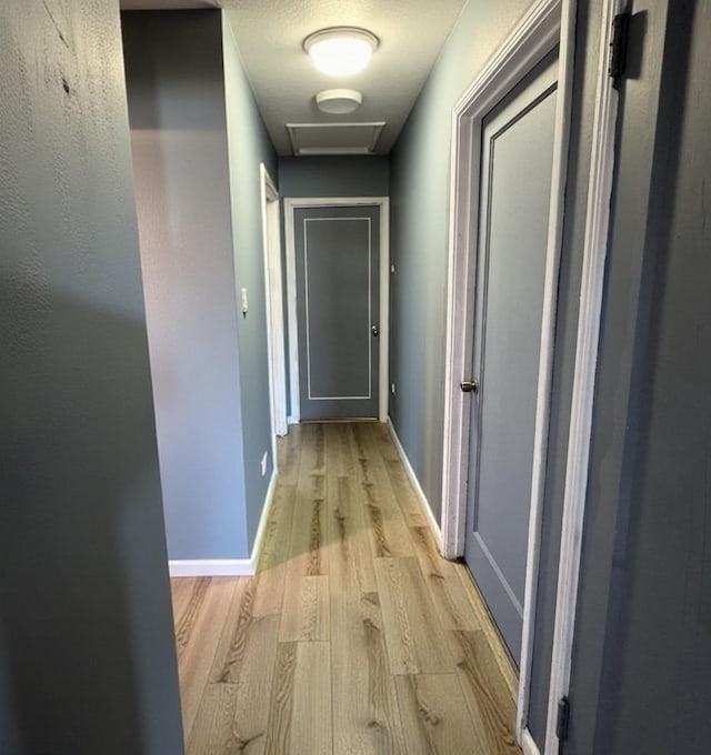 hall featuring light wood-style floors, attic access, and baseboards