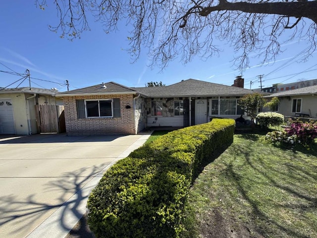 single story home featuring brick siding, a shingled roof, concrete driveway, fence, and a front yard