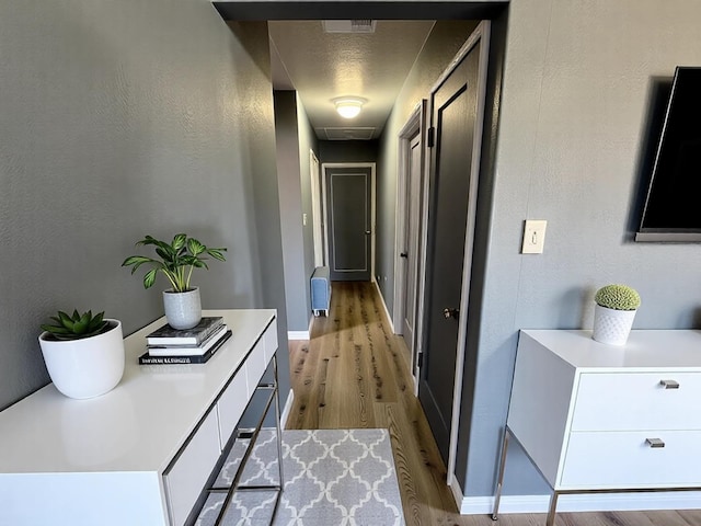 hallway featuring a textured wall, wood finished floors, visible vents, and baseboards