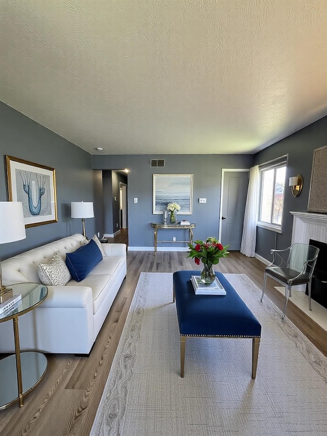 living room with a fireplace, wood finished floors, visible vents, and baseboards