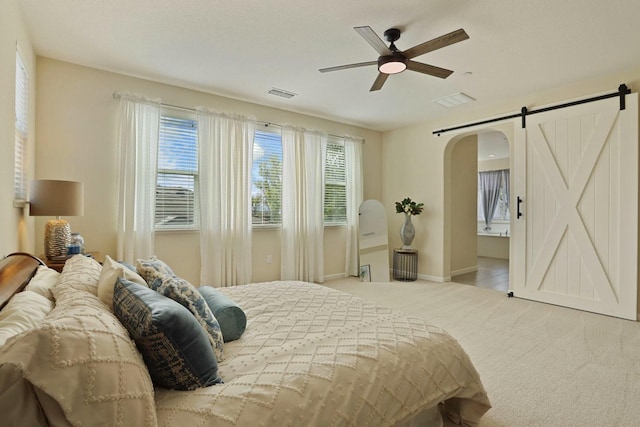 carpeted bedroom with arched walkways, visible vents, multiple windows, and a barn door