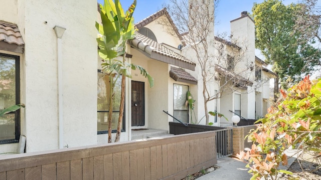 exterior space with stucco siding, a tiled roof, a chimney, and fence