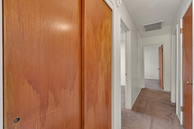 hall with visible vents, a textured ceiling, and carpet flooring