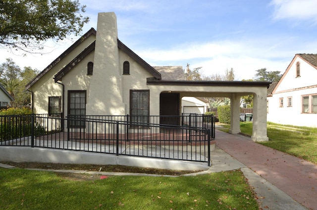 view of front facade with stucco siding, fence, a front yard, a shingled roof, and a chimney