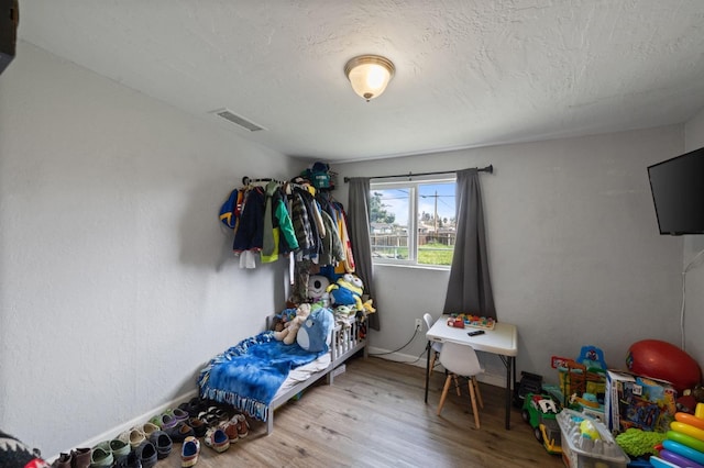 bedroom featuring visible vents, a textured ceiling, baseboards, and wood finished floors