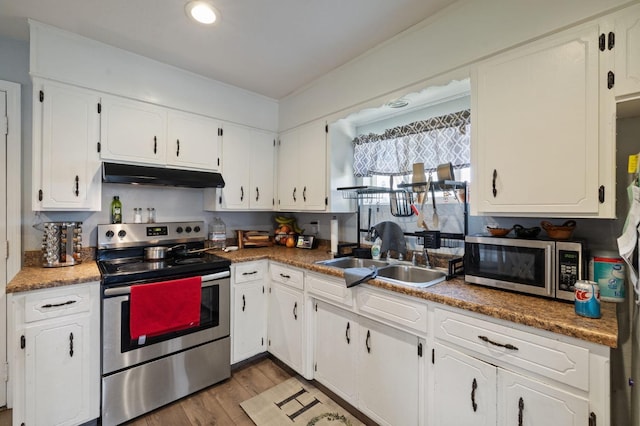 kitchen with under cabinet range hood, a sink, wood finished floors, appliances with stainless steel finishes, and white cabinets