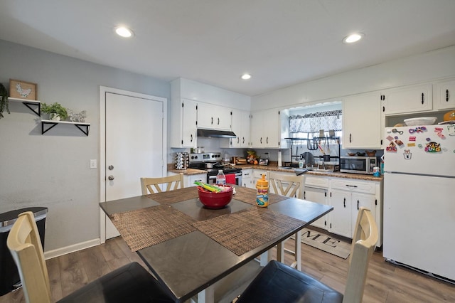 kitchen with wood finished floors, recessed lighting, under cabinet range hood, appliances with stainless steel finishes, and white cabinetry