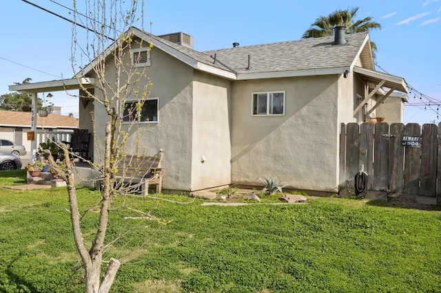 rear view of property featuring a lawn, fence, roof with shingles, and stucco siding