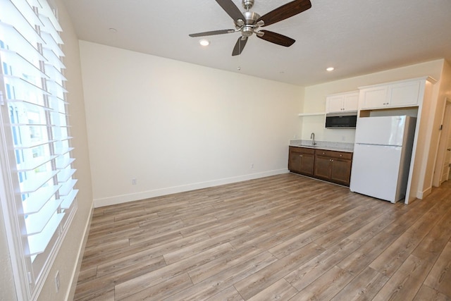 kitchen featuring baseboards, freestanding refrigerator, a sink, stainless steel microwave, and light wood-type flooring